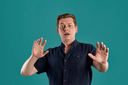Close-up portrait of a ginger guy in navy t-shirt posing on blue background. Sincere emotions.
