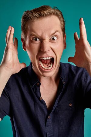 Close-up portrait of a ginger guy in navy t-shirt posing on blue background. Sincere emotions.