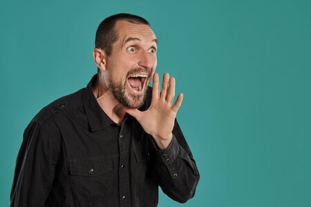 Middle-aged man with beard and mustache, wears black shirt, posing against a blue background....