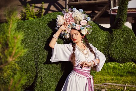 Brunette girl in a white ukrainian authentic national costume and a wreath of flowers is posing...