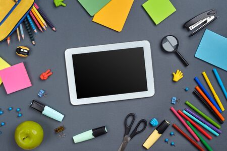 Flat lay photo of workspace desk with school accessories or office supplies on gray background.