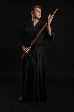 Kendo guru wearing in a traditional japanese kimono is practicing martial art with the shinai bamboo sword against a black studio background.の写真素材