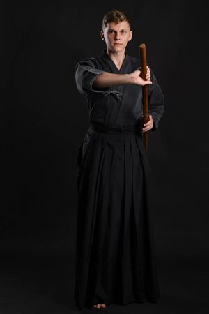 Kendo guru wearing in a traditional japanese kimono is practicing martial art with the shinai bamboo sword against a black studio background.の写真素材