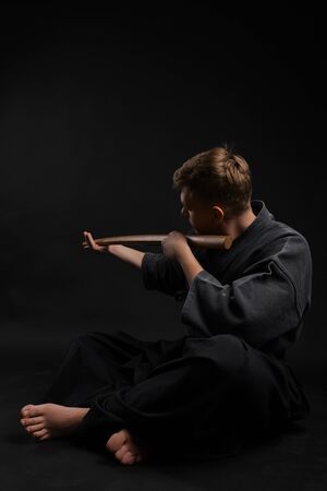 Kendo guru wearing in a traditional japanese kimono is practicing martial art with the shinai bamboo sword against a black studio background.の写真素材