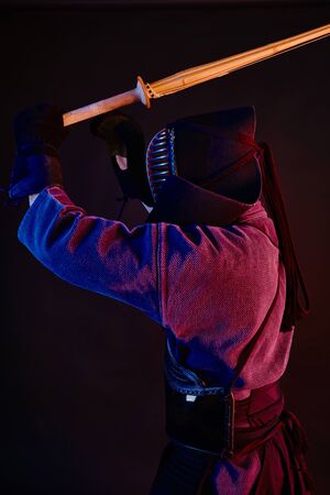 Athletic Kendo instructor wearing in an armor, traditional kimono and helmet is practicing martial...