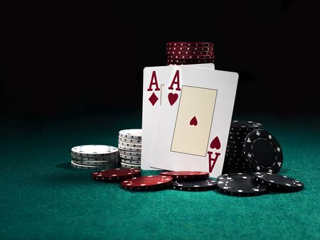 Two aces hearts and diamonds standing leaning on chips piles, some of them laying nearby on green...