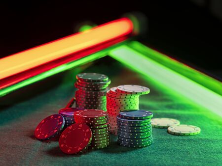 Close-up shot of a colorful chips piles, some of them laying nearby on green cover of playing table, under green and red neon lights. Black background. Close-up.の写真素材