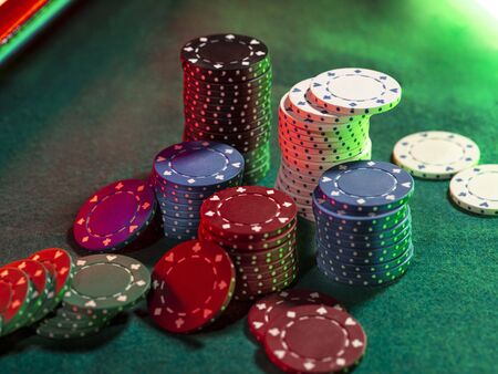 Close-up top view of colorful chips piles, some of them laying nearby on green cover of playing...