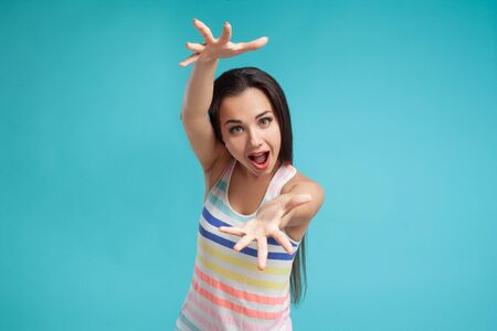 Brunette woman with long hair, dressed in colorful striped shirt, posing against blue studio...