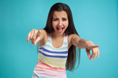Brunette woman with long hair, dressed in colorful striped shirt, posing against blue studio background. Sincere emotions. Close-up.の写真素材