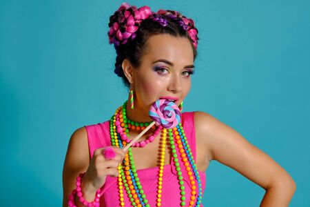 Lovely girl with a multi-colored braids hairstyle and bright make-up, posing in studio against a...