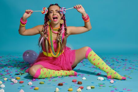 Lovely girl with a multi-colored braids hairstyle and bright make-up, posing in studio with...