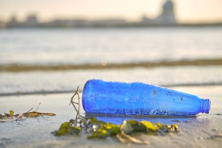 Used blue glass bottle lies on the river shore, next to the algae. Cleaning up trash. People and...
