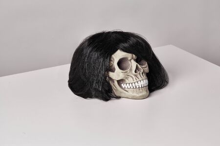 Realistic model of a human skull with teeth in a black wig on a light table, white background. Medical science or Halloween horror concept. Close-up shot.の写真素材