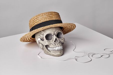 Realistic model of a human skull with teeth in a yellow straw hat and headphones on a light table, white background. Medical science or Halloween horror concept. Close-up shot.の写真素材