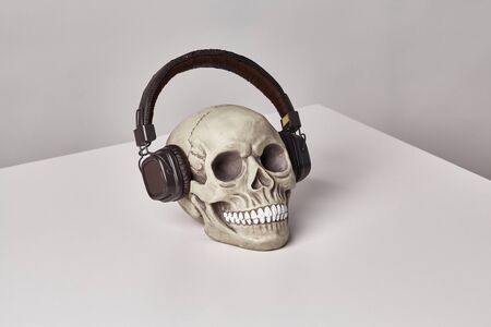 Realistic model of a human cranium with teeth in a black headphones on a light table, white background. Medical science or Halloween horror concept. Close-up shot.の写真素材