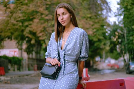 Blonde girl in long blue dress and a small black handbag on her shoulderの写真素材