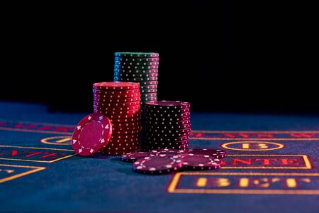 Colored chips piles are located on a blue cover of a playing table with markup, some of them are...