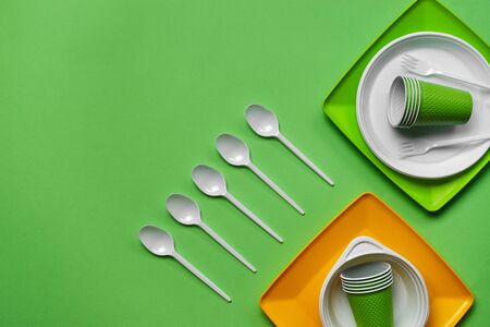 Colorful plastic disposable cutlery, such as plates, five spoons, two forks and bowls on green...