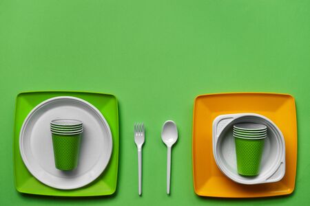 Colorful plastic disposable tableware, such as plates and bowls, spoon, fork on green background with copy space. The concept of picnic utensil. Also used in fast food restaurants, takeaways. Top view. Selective focus. Close-up shot.の写真素材