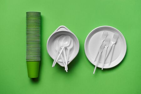 Colorful plastic disposable tableware, such as plates, spoons, forks and folded cups on green...