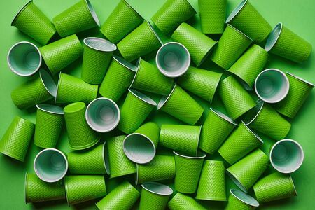 Green plastic disposable tableware, such as a lot of cups on green background with copy space. The concept of picnic utensil. Also used in fast food restaurants, takeaways. Top view. Selective focus. Close-up shot.の写真素材