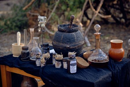 Table with accessories for spells and witchcraft standing in a pine forest. Magic potion is brewed...