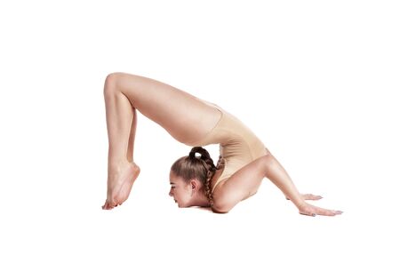 Flexible girl gymnast in beige leotard is performing complex elements of gymnastics while posing isolated on white background. Close-up.の写真素材