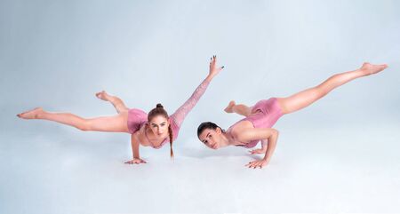 Two flexible girls gymnasts in beige leotards performing complex elements of gymnastics using...