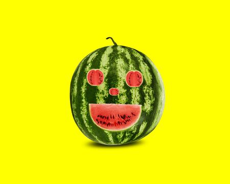 Green, striped, emoticon carved out in watermelon on yellow background with copy space for text, images. Berry with pink flesh. Side view. Close-up.の写真素材