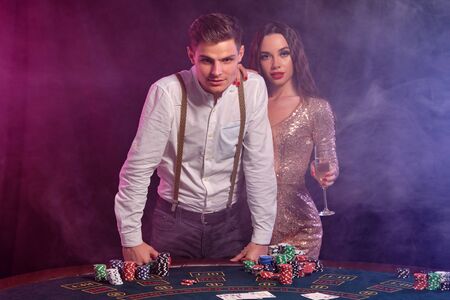 Man and woman playing poker at casino, celebrating win at table with stacks of chips, cards, champagne. Black, smoke background. Close-up.の写真素材