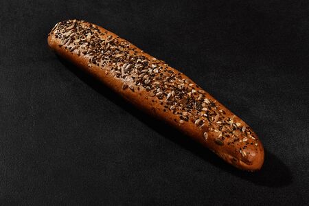 Fresh, tasty baked bread sprinkled with sesame and sunflower seeds against black