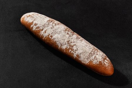Fresh, delicious baked bread sprinkled with flour against black background with copy space. Rural...