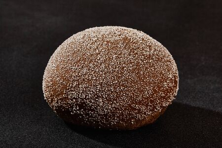 Fresh, palatable baked bun sprinkled with ground coconut against black