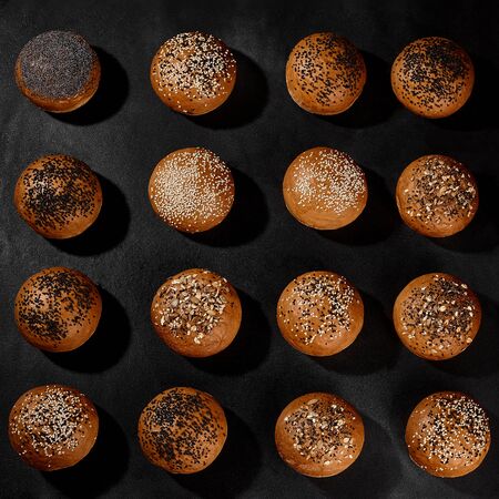Variety of fresh, tasty baked buns with black and white sesame and sunflower seeds against blackの写真素材