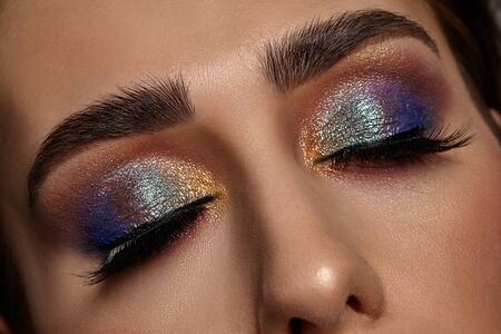 Face of a girl with luxury makeup and perfect skin. She has closed her eyes. Blue and golden eyeshadow, false eyelashes and brown eyebrows. Professional maquillage. Close upの写真素材