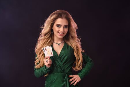 Blonde girl in green stylish dress and jewelry. Put her hand on hip, smiling, showing two aces,...