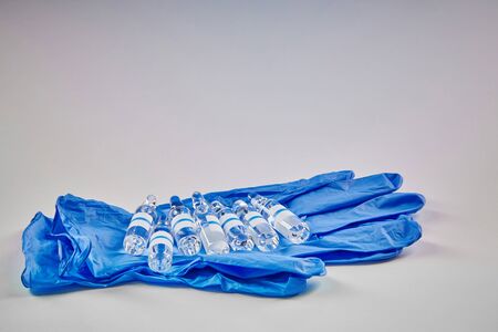 Seven mockup ampoules with transparent liquid on blue disposable gloves isolated on white. Laboratory research of Coronavirus. Worldwide pandemic COVID-19, 2019-nCoV, SARS-CoV-2. Close upの写真素材