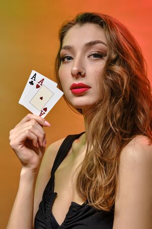 Brunette woman with earring in nose, in black dress. Showing two aces, posing on colorful...