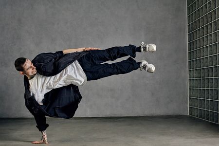 Guy with tattooed body, beard. Dressed in white t-shirt and sneakers, black shirt, pants. Showing tricks on gray background. Dancehall, hip-hopの写真素材