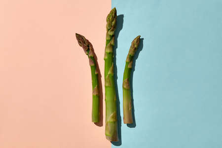 Three fresh organic asparagus stems on pink and blue background. Concept of healthy nutrition, food and seasonal vegetables harvest. Close upの写真素材