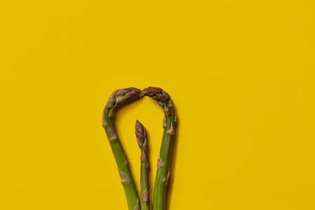 Raw fresh green asparagus stalks over yellow background. Concept of food and seasonal vegetables harvest. Close up, copy spaceの写真素材