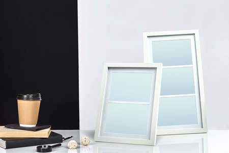 Two blank frames, paper cup of coffee on books and magnifier on tabletop against black and white...