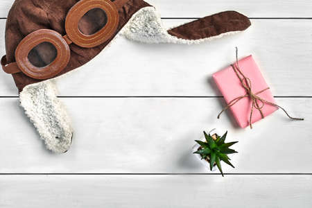 Warm brown hat, pink gift box tied by jute thread and green succulent in a pot on white wooden...