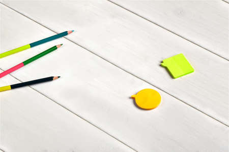 Colorful double-sided pencils, orange and yellow sticky notes on white wooden desktop or background....