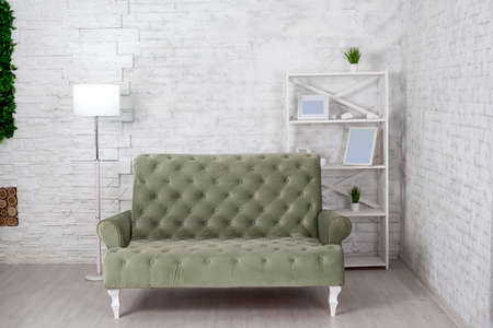 Living room interior with gray sofa against white brick wall. Modern lamp, shelving with empty photo...