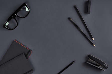 Two black notepads, glasses, pencils and stapler on dark gray background. Stationery, supplies for...