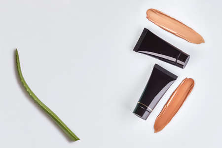Two black tubes of tone cream, foundation smeared by surface, green leaf of aloe isolated on white. Cosmetic packaging. Close up, copy spaceの写真素材