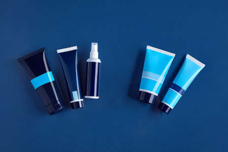 Four colorful different sized tubes and pump bottle with no logo against blue background. Cosmetic...