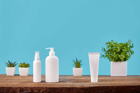 One white tube and two pump bottles with no logo on wooden tabletop against green plants in pots and...
